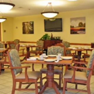 A warmly lit dining area with neatly arranged tables and chairs, featuring artwork on the walls.