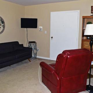 A cozy living room featuring a black sofa, red armchair, wall-mounted television, and a clock.