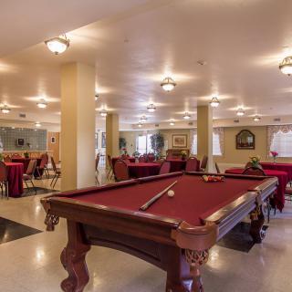 A well-lit recreation room featuring a billiards table and seating area.