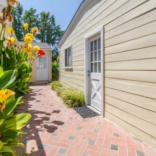 A sunny walkway beside a house, lined with colorful flowers and greenery.