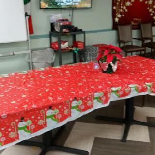 A festive setup for a holiday gathering, featuring a red tablecloth adorned with Christmas-themed designs and a poinsettia plant as a centerpiece.