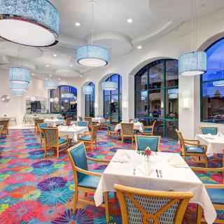 A vibrant restaurant interior with colorful carpet, modern furnishings, and large windows.