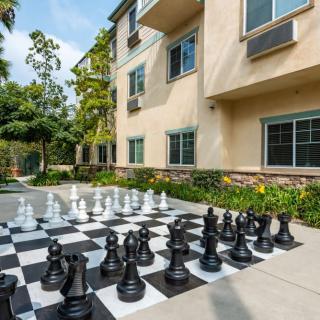 An outdoor setting featuring a giant chessboard with large black and white chess pieces, situated next to a residential building.