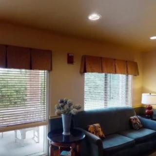 A cozy living room with a sofa, windows with blinds, and a side table holding a vase of flowers.