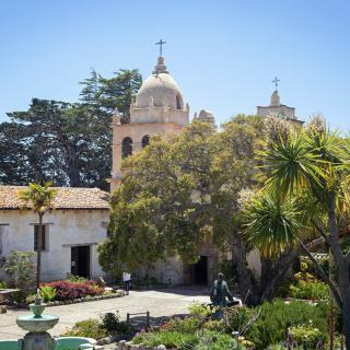 Historic mission church surrounded by trees and a fountain in California.