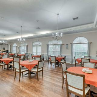 A spacious dining room with tables covered in orange tablecloths and elegant chandeliers.