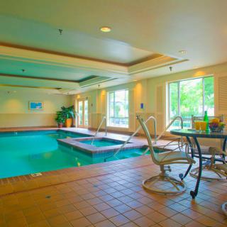 A serene indoor swimming pool area with a connected spa, surrounded by natural light and comfortable seating.