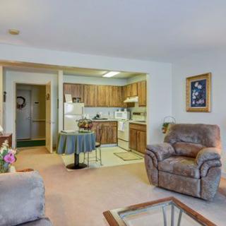 A cozy living room with an open view of the kitchen, featuring comfortable armchairs and a small dining table.