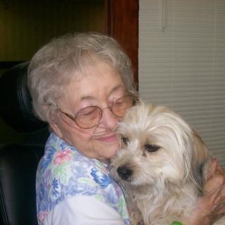 An elderly woman hugging a small dog indoors, both looking content.