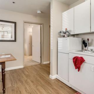 A compact kitchen with integrated laundry facilities, featuring white cabinets and wood flooring.