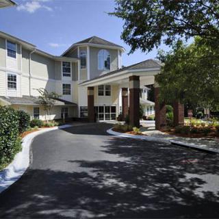 A view of a building entrance with a driveway and surrounding trees.