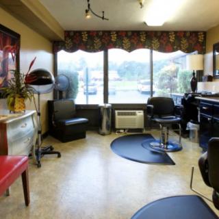 A cozy hair salon interior with chairs, a large window, and styling equipment.