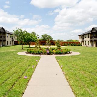 A serene garden with a central circular planter surrounded by grass and flanked by buildings on either side.