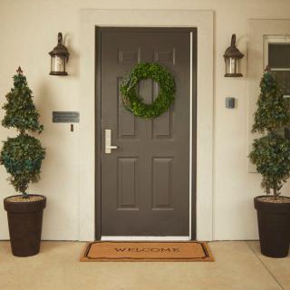 A welcoming front door adorned with a wreath, flanked by potted plants and lanterns.