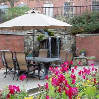 A cozy garden patio with outdoor seating, a large umbrella, vibrant flowers, and a small fountain.
