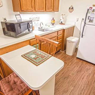 A small kitchen with wooden cabinets, a microwave, and a refrigerator, featuring a table and chairs.