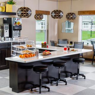 A modern kitchen with an island counter, stylish bar stools, and a display of pastries under geometric pendant lights.