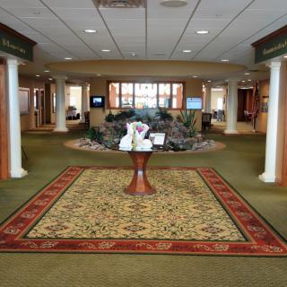 A spacious lobby with a decorative centerpiece on a round table, flanked by columns and featuring a green carpet.