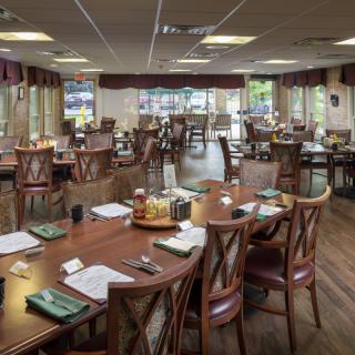 An empty restaurant dining area with neatly arranged tables and chairs, surrounded by large windows.