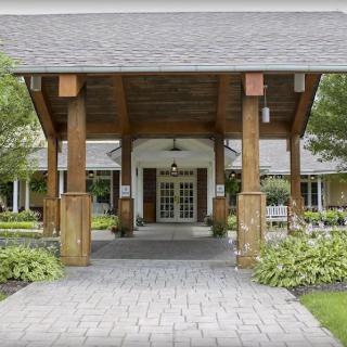 A welcoming entrance with wooden pillars and a paved pathway, surrounded by lush greenery.