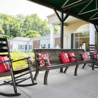A cozy outdoor seating area with a rocking chair and benches adorned with red cushions, next to a building.