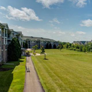 A scenic view of apartment buildings alongside a grassy open field with a pathway under a clear blue sky.