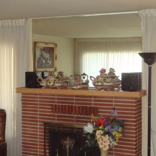 A cozy living room with a brick fireplace, decorated with floral arrangements and flanked by speakers, underlined by elegant curtains.