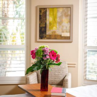 A cozy room interior with a vase of colorful flowers on the table, surrounded by chairs and illuminated by natural light through the windows.