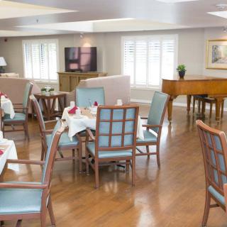 An empty dining room with neatly arranged tables and chairs, featuring a piano in the corner.