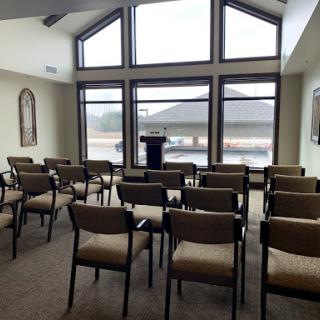 A vacant meeting room featuring rows of chairs and a podium, illuminated by natural light from large windows.