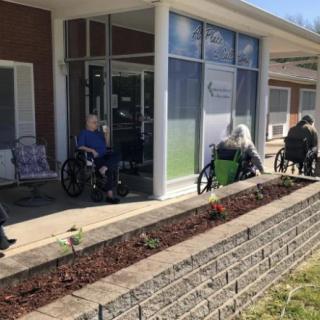 Elderly individuals sitting in wheelchairs outside a nursing home during the daytime.