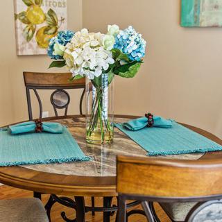 A cozy dining setup with a wooden table, adorned with a vase of white and blue flowers and teal placemats.