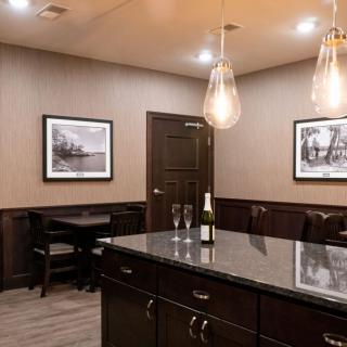 A modern kitchen interior featuring a large island with a wine bottle and glasses, illuminated by pendant lights and decorated with framed artwork.