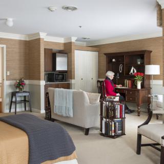 A cozy living space featuring a seating area, bookshelf, and a desk with a person seated.