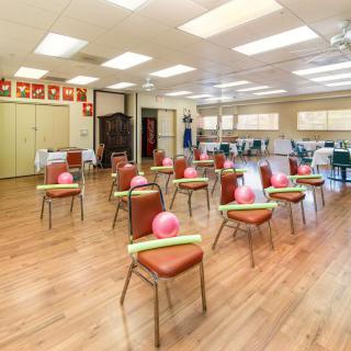 A brightly lit exercise room with chairs arranged in rows, each topped with a balloon and pool noodle.
