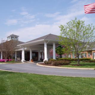 A building entrance with white columns, an American flag, and landscaped surroundings.