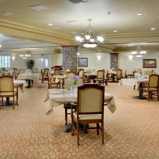 An elegant dining room with neatly arranged tables and chairs, illuminated by chandeliers.