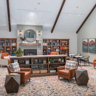 A cozy living room with a fireplace and bookshelves, featuring armchairs and a patterned rug.