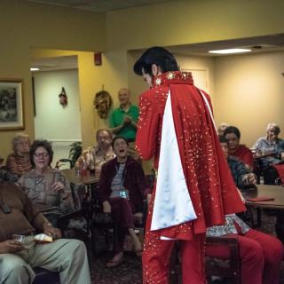 A performer in a red costume entertains an audience indoors.