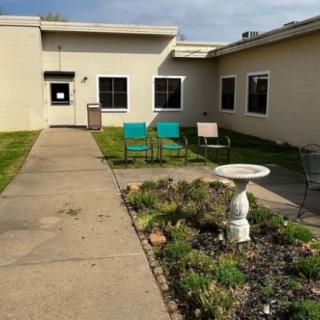 A view of an outdoor area featuring a pathway, garden, and chairs in front of a building.