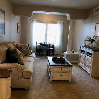 A cozy living room with a sofa, coffee table, and adjacent dining area, featuring warm lighting and elegant decor.