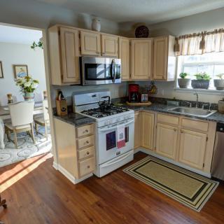 A cozy kitchen with wooden cabinets, a stove, and a microwave, leading into a dining area adorned with plants.