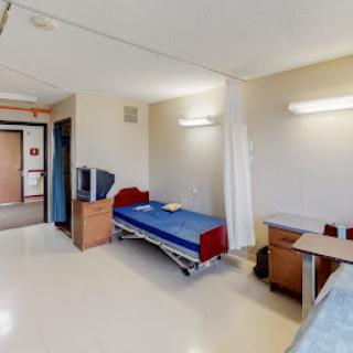 A simple and clean patient room in a hospital, equipped with a bed, desk, and television.
