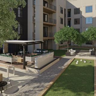 A modern apartment building courtyard featuring green landscaping and patio seating.