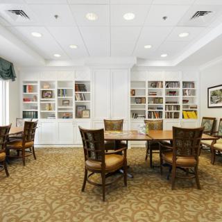 A cozy library interior with tables and chairs for reading or meetings, surrounded by bookshelves.