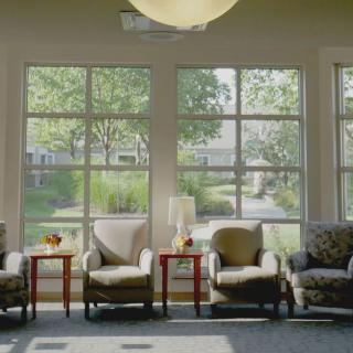 A sunny waiting room with comfortable chairs and tables by large windows.