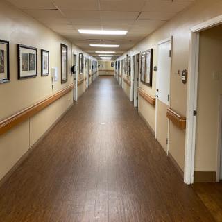 A well-lit corridor lined with photographs, featuring a wooden floor and multiple doors on either side.