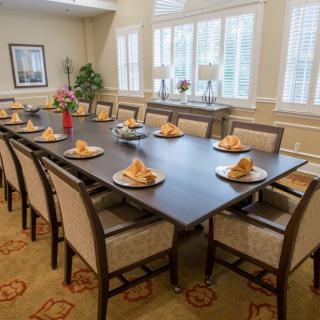 A well-appointed dining room with a large table set for a formal gathering, featuring elegant chairs and neatly placed napkins.