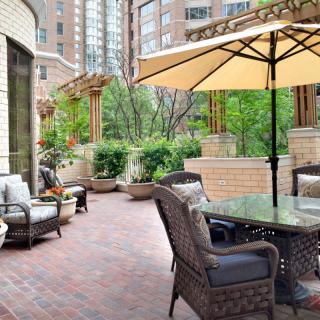A cozy outdoor patio with comfortable furniture and a large umbrella amidst an urban backdrop.