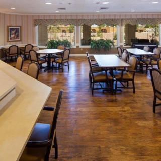 A spacious dining area with several tables and chairs, featuring large windows and a wooden floor.
